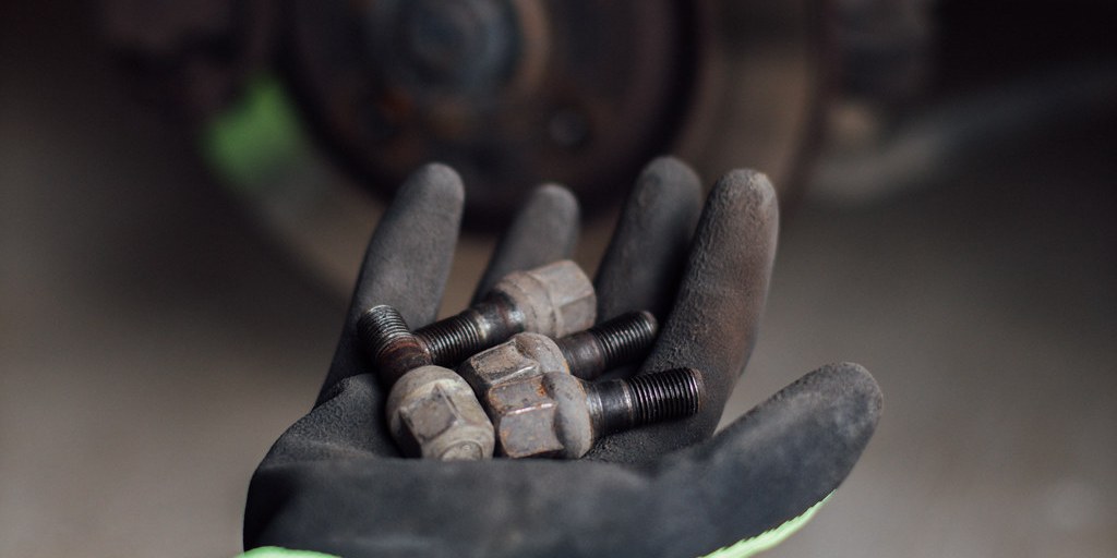 Mechanic's gloved hand holding wheel bolts in front of the brake rotor during inspection